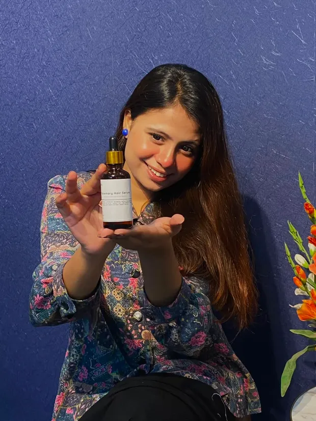 ফুলেল প্রিন্টের জ্যাকেট পরা তরুণী হাসিমুখে The Formulate হেয়ার সিরাম দেখাচ্ছেন